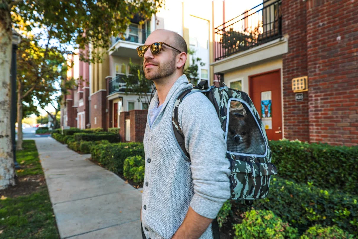 A man seen smiling while walking around the city carrying a Petique modern pet backpack with his small dog sitting inside.